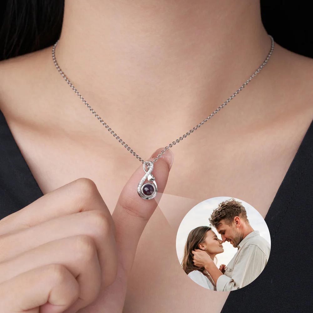 Silver infinity hidden photo necklace worn, finger holding pendant showing projected couple picture under light