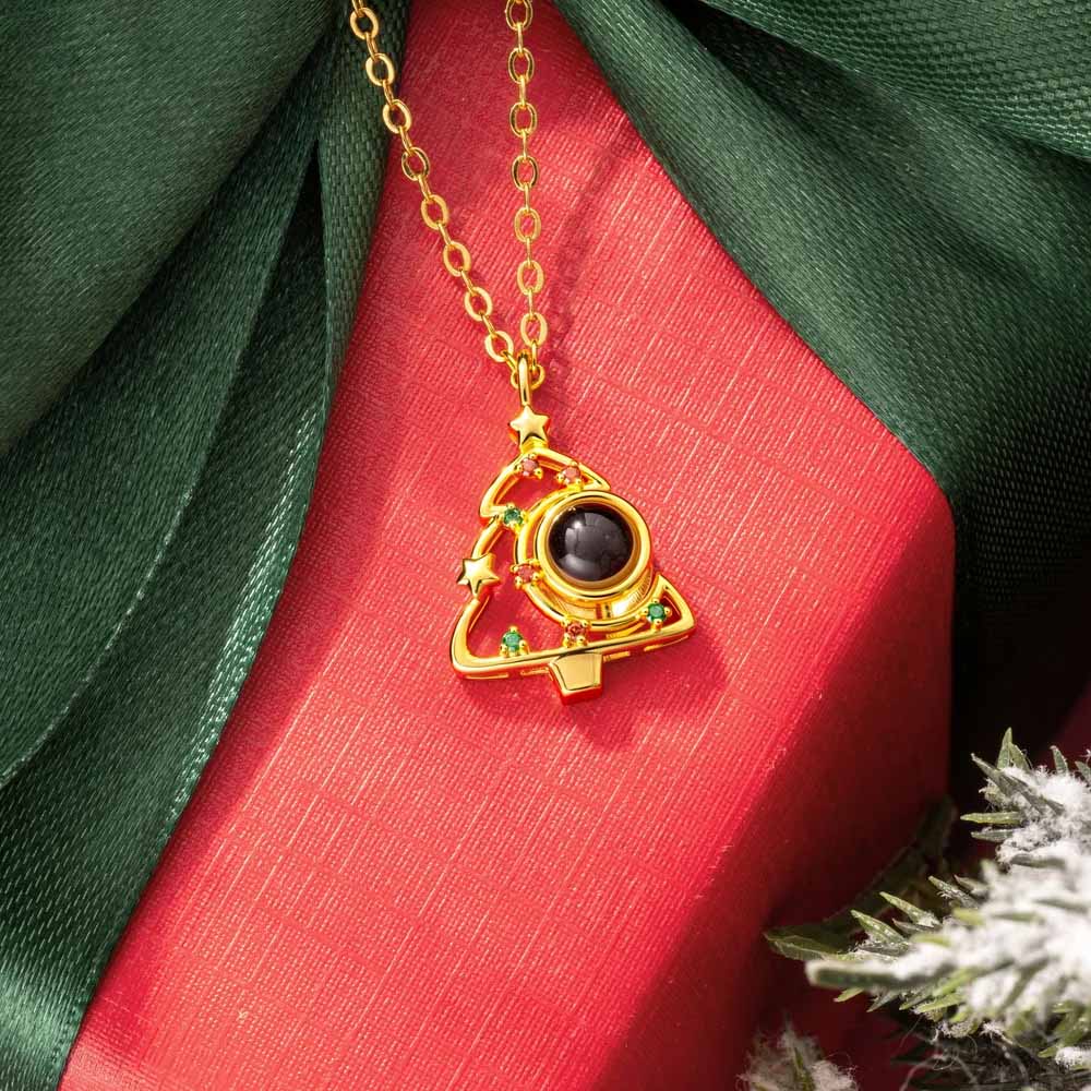 Gold Christmas tree projection necklace on red gift box with green ribbon, festive holiday flat lay