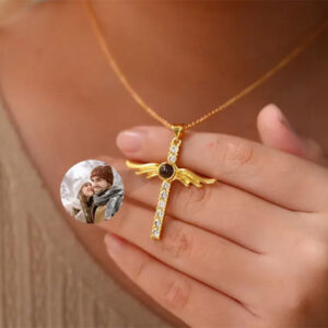 Gold angel wings cross necklace held in hand, showing projected winter couple photo inside crystal