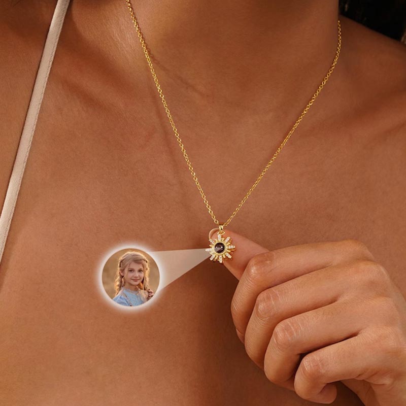 Gold sun projection necklace held by finger, showing projected little girl photo inside crystal