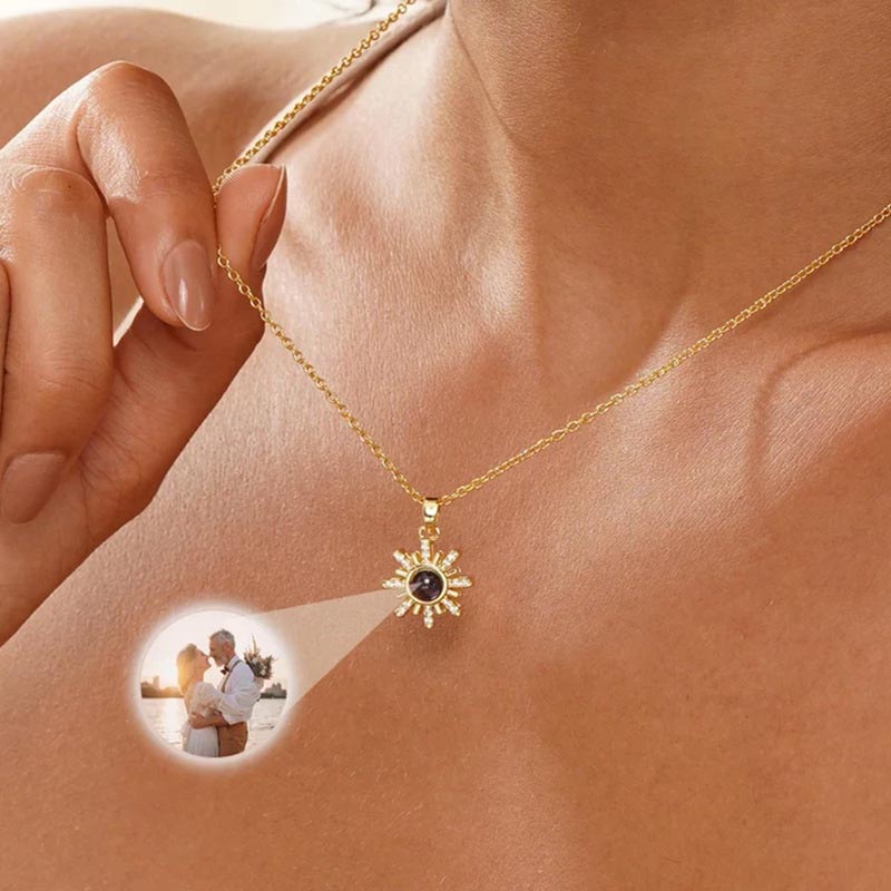 Gold sunshine necklace held in hand, sunset couple photo projecting from center sun crystal
